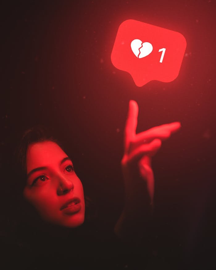 Red-hued image of a woman reaching towards a broken heart icon symbolizing digital detachment.