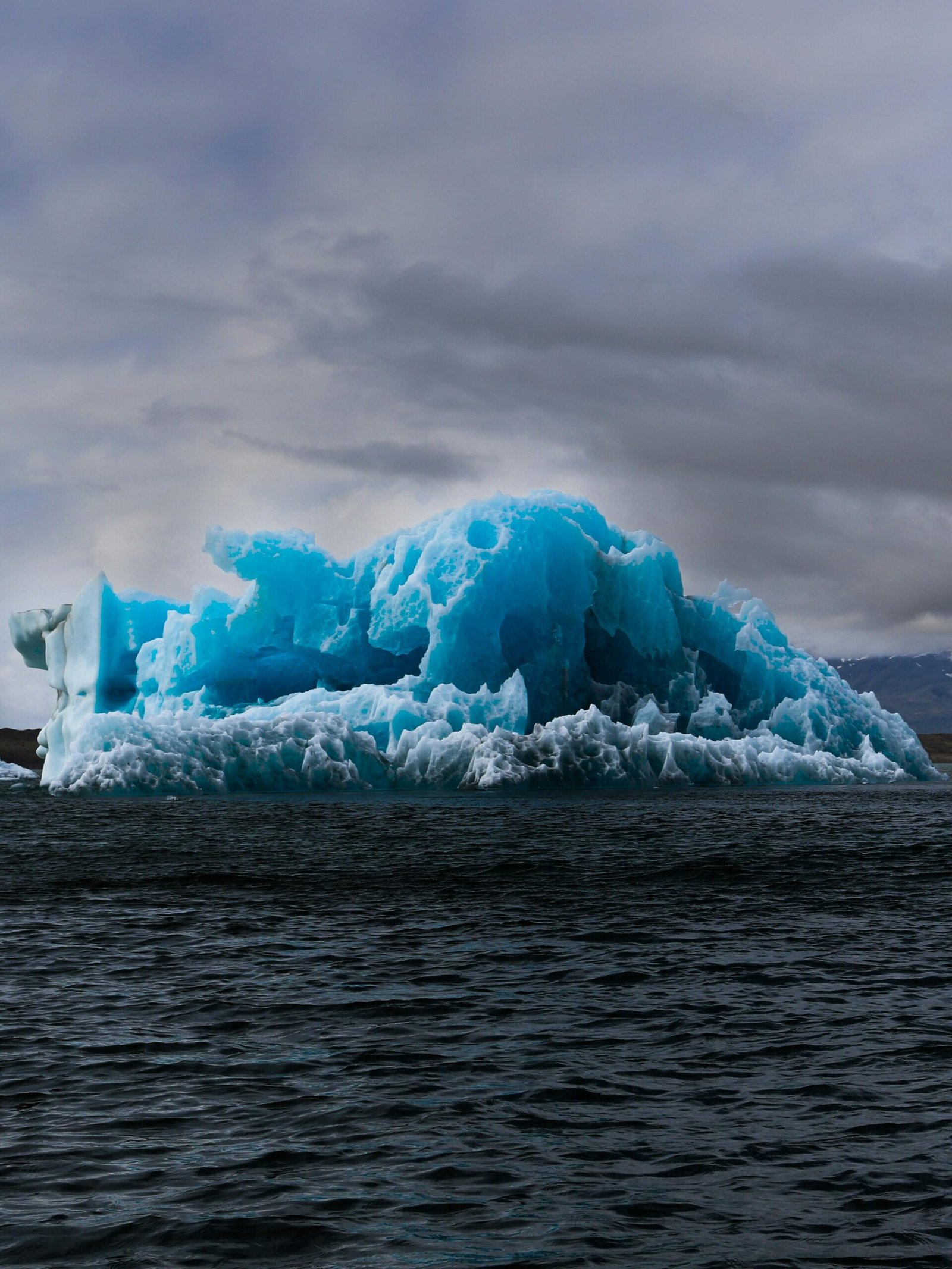 Stunning blue iceberg in calm waters under a cloudy sky, showcasing nature's beauty.