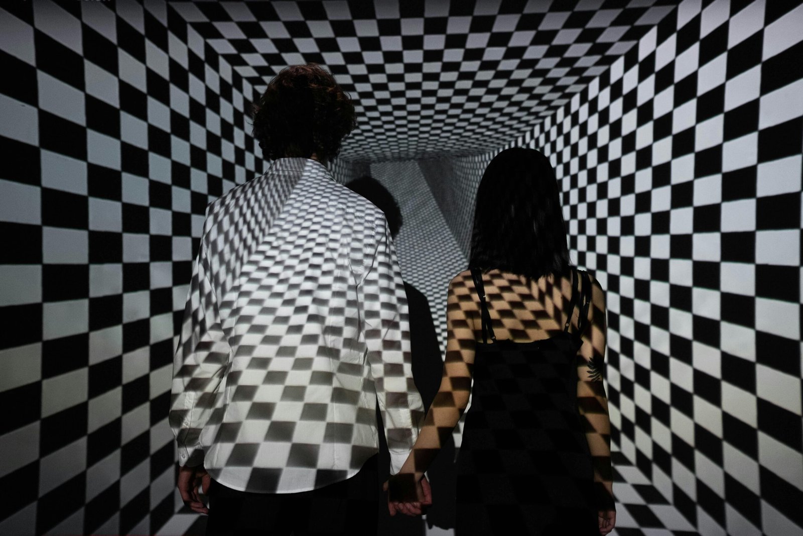 Couple walking in a checkerboard tunnel, creating an optical illusion of depth and connection.