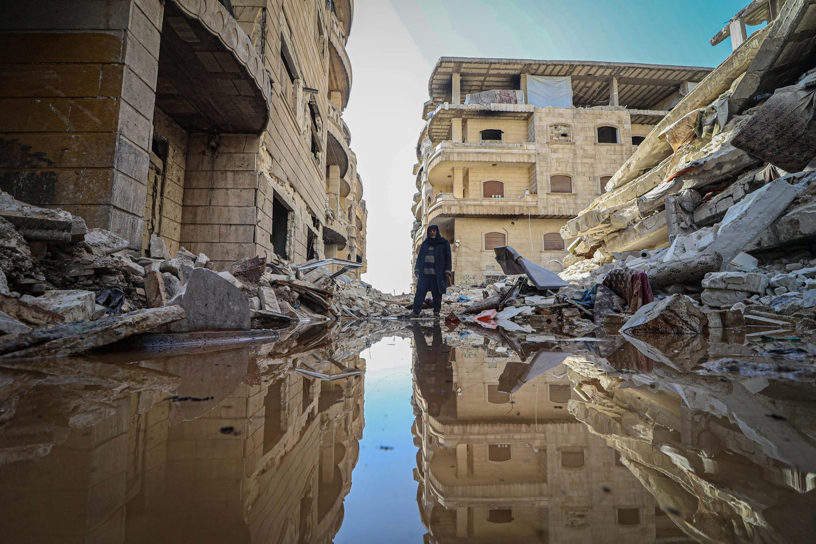 A man stands amidst earthquake devastation in Idlib, Syria, reflecting on destruction.