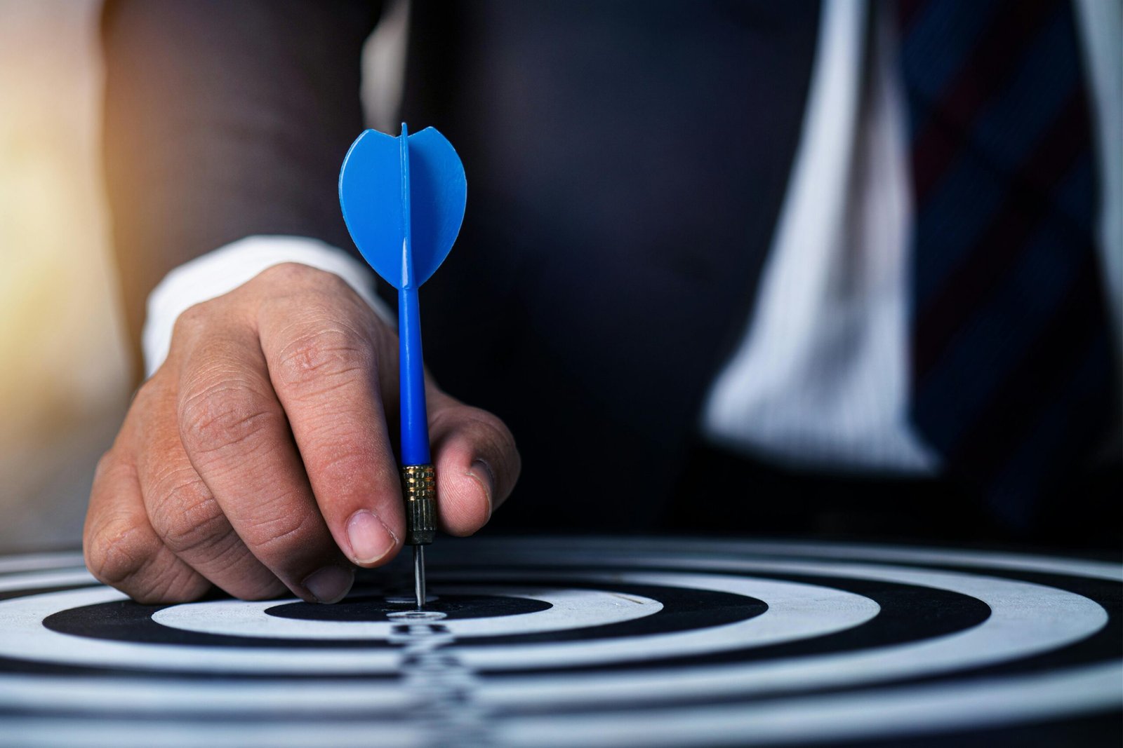 Global risks do not hit companies directly. They hit decision systems Close-up of a man's hand holding a blue dart on a bullseye, symbolizing precision and focus.