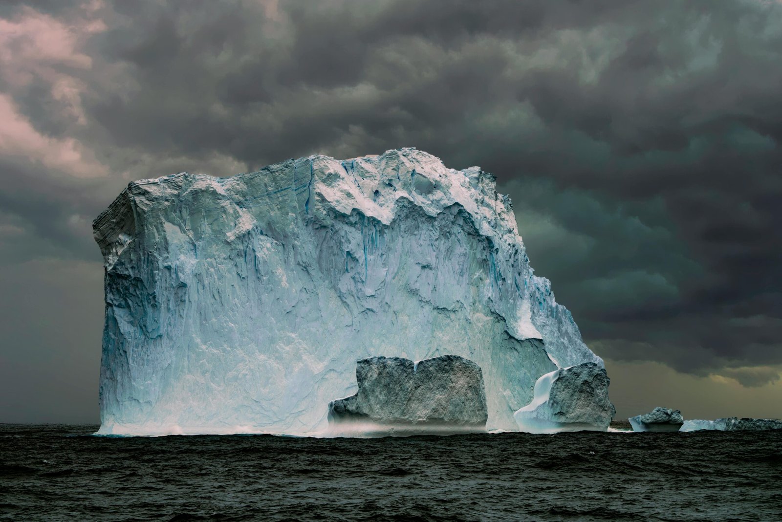 A massive iceberg floating in the sea with dramatic storm clouds overhead, showcasing nature's power.