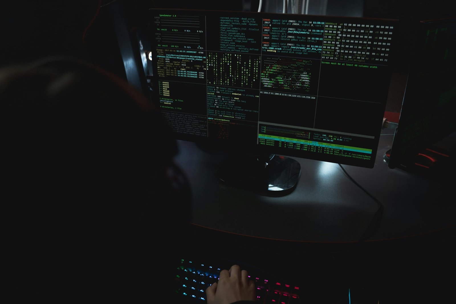 Dark room setup with code displayed on PC monitors highlighting cybersecurity themes.