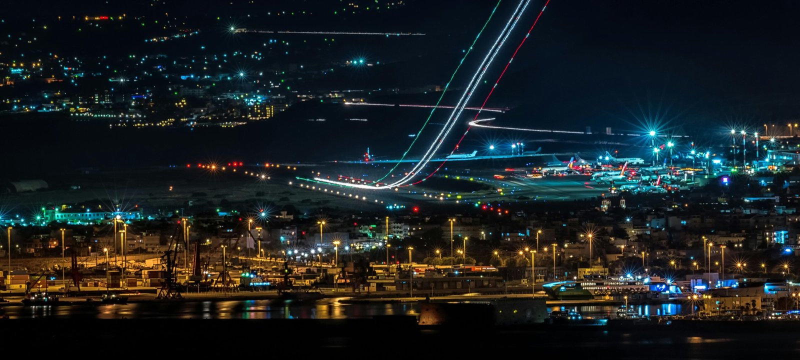 A vibrant cityscape featuring a busy airport and harbor with bright lights at night.